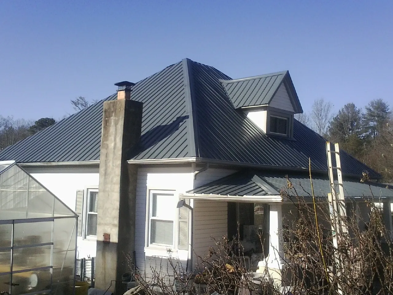 Dark blue standing seam metal roof on a white farmhouse with dormer — Slate & Tile Roof Repair by Roofing Brothers in Pine Valley