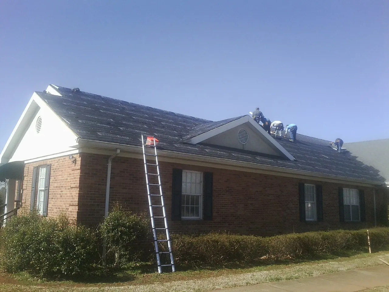 Crew tearing shingles off a brick ranch roof with a ladder set — Metal Roof Repair work by our crew in Pine Valley