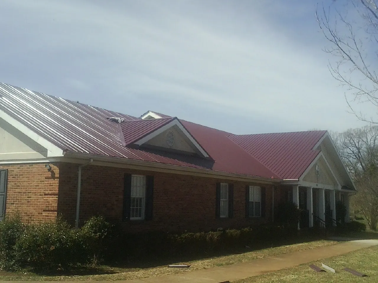 Red metal roof with gabled entries on a long brick building, from a Hail Damage Roof Repair job in Pine Valley