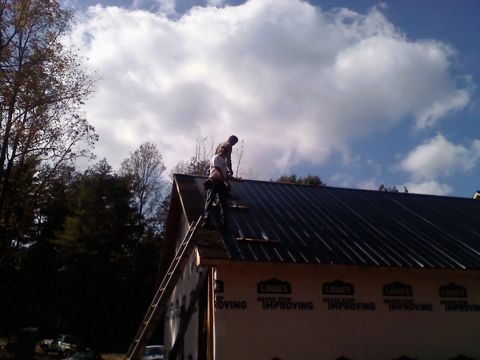 Roofer fastening dark metal panels high against a cloudy sky, from a Roof Inspection job in Pine Valley